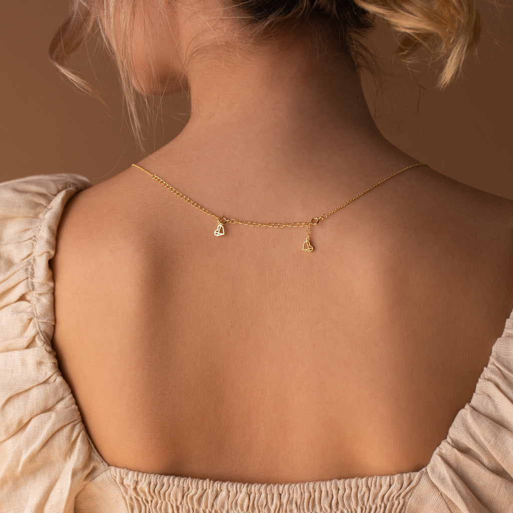 A woman in a low-back dress wears a gold necklace with small heart charms resting on her upper back, styled with the Chain Extender in Sterling Silver for an adjustable, perfect fit.