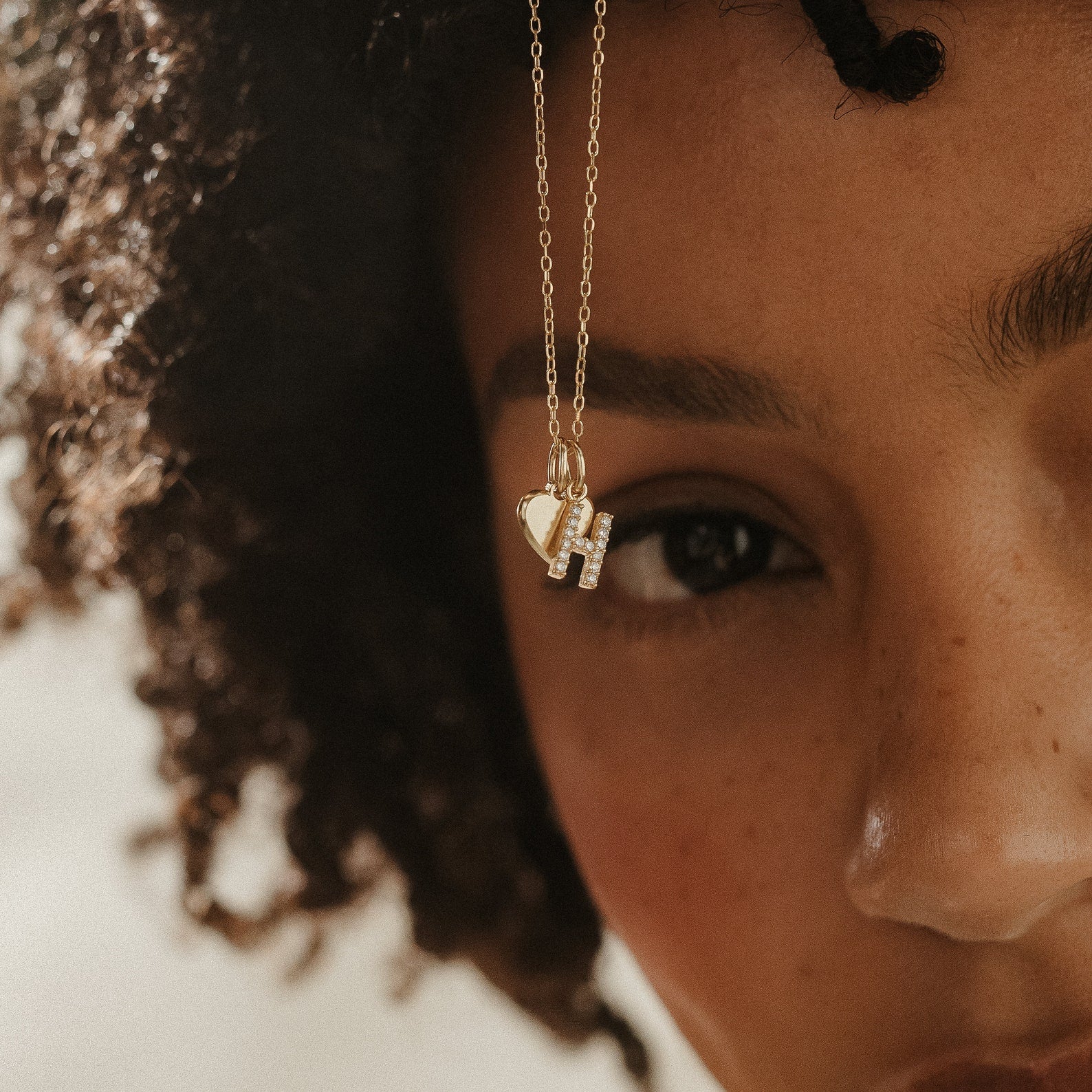 A close-up of a woman wearing the Pave Initial Heart Necklace, featuring a gold pendant with a heart charm and the letter H, elegantly highlighting her unique style.