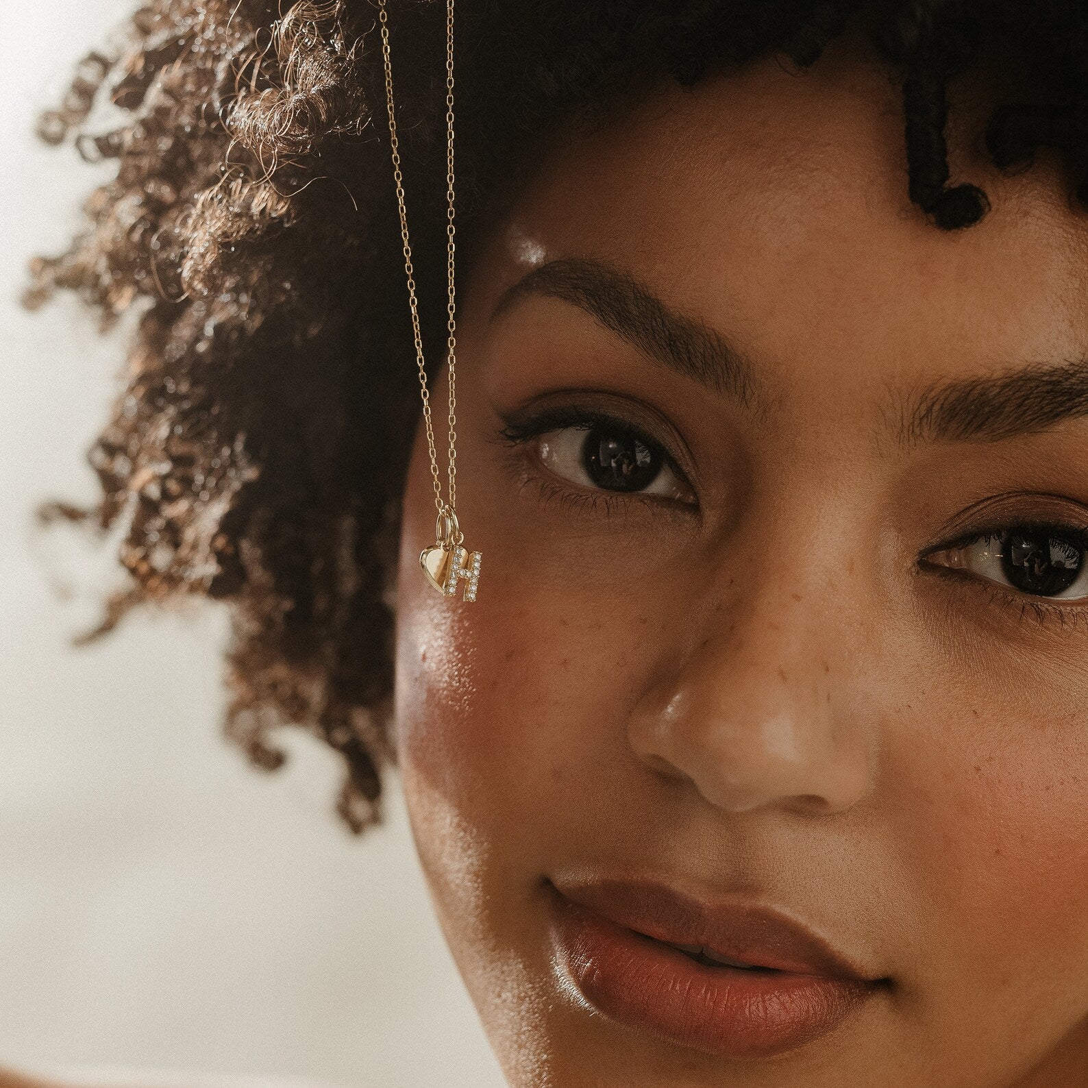 Close-up of a woman with curly hair wearing the Pave Initial Heart Necklace near her face.