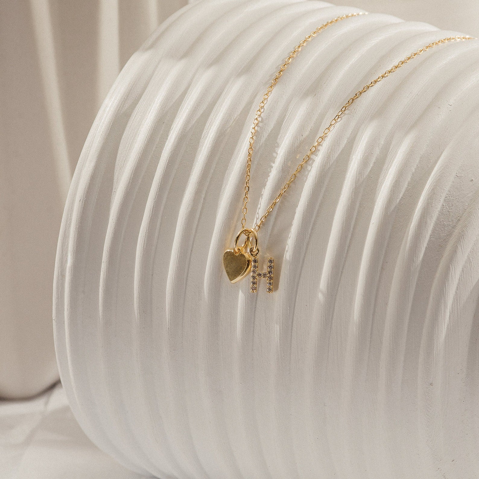 Pave Initial Heart Necklace featuring a gold heart charm and initial pendant with rectangular accents, elegantly displayed on a textured white surface.