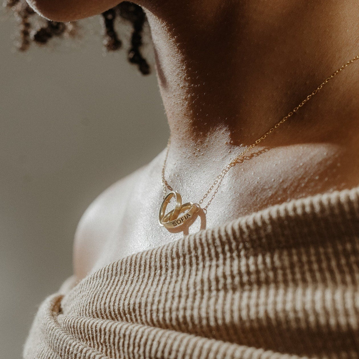Close-up of a woman's neck wearing the Engraved Interlocking Necklace, featuring gold interlocking circles and a pendant engraved with "Sofia"—an ideal personalized anniversary gift.