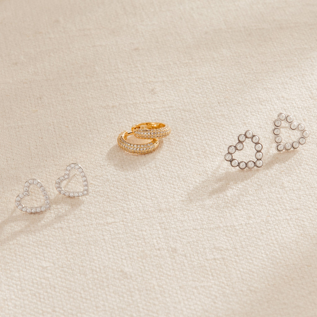 A row of heart-shaped earrings, the Clarissa Pave Huggies, and a pair of gold earrings—perfect additions to your date night jewelry collection.