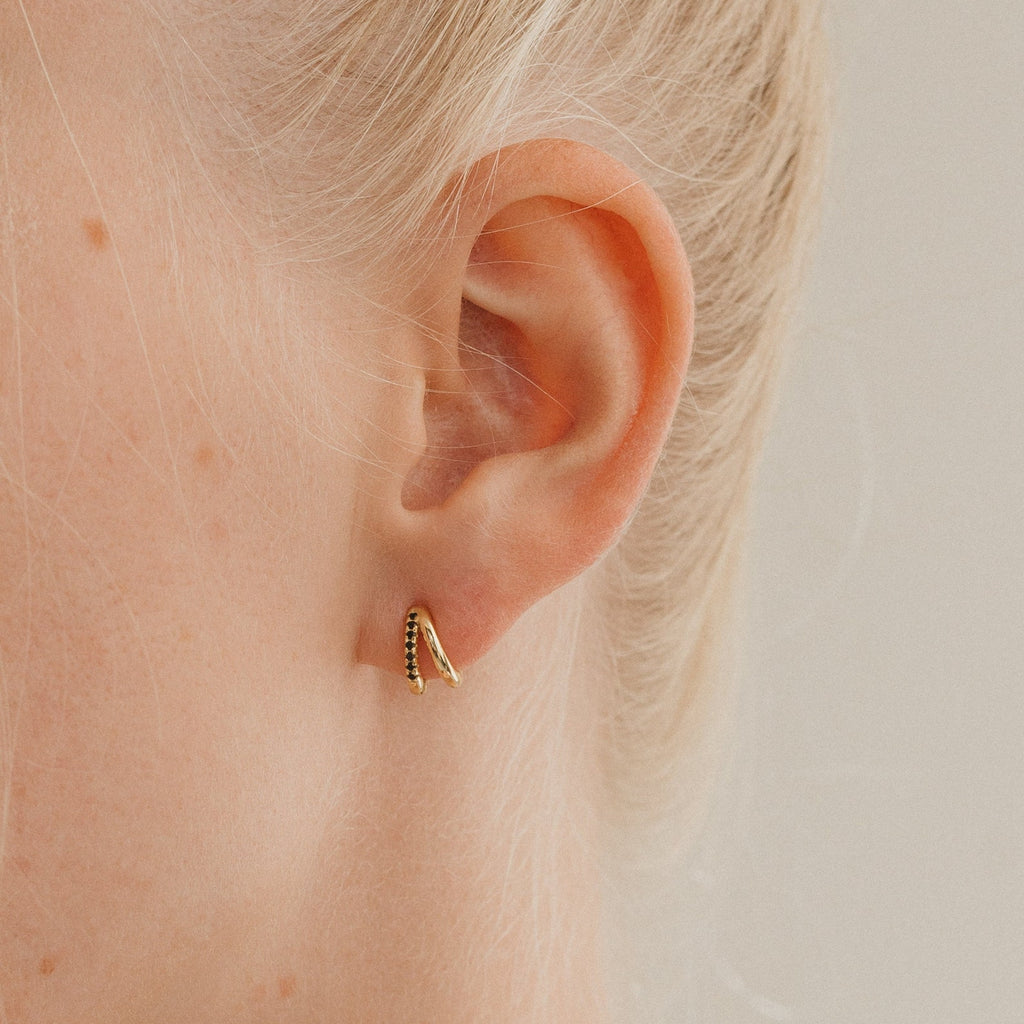 Close-up of an ear wearing the Amelia Onyx Duo Huggies—minimalist small gold hoops with black detailing, ideal for those who love onyx-inspired earrings.