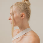 A woman with blonde hair in a bun, wearing a white top and the elegant Arabella Diamond Studs, is seen in profile against a plain background.
