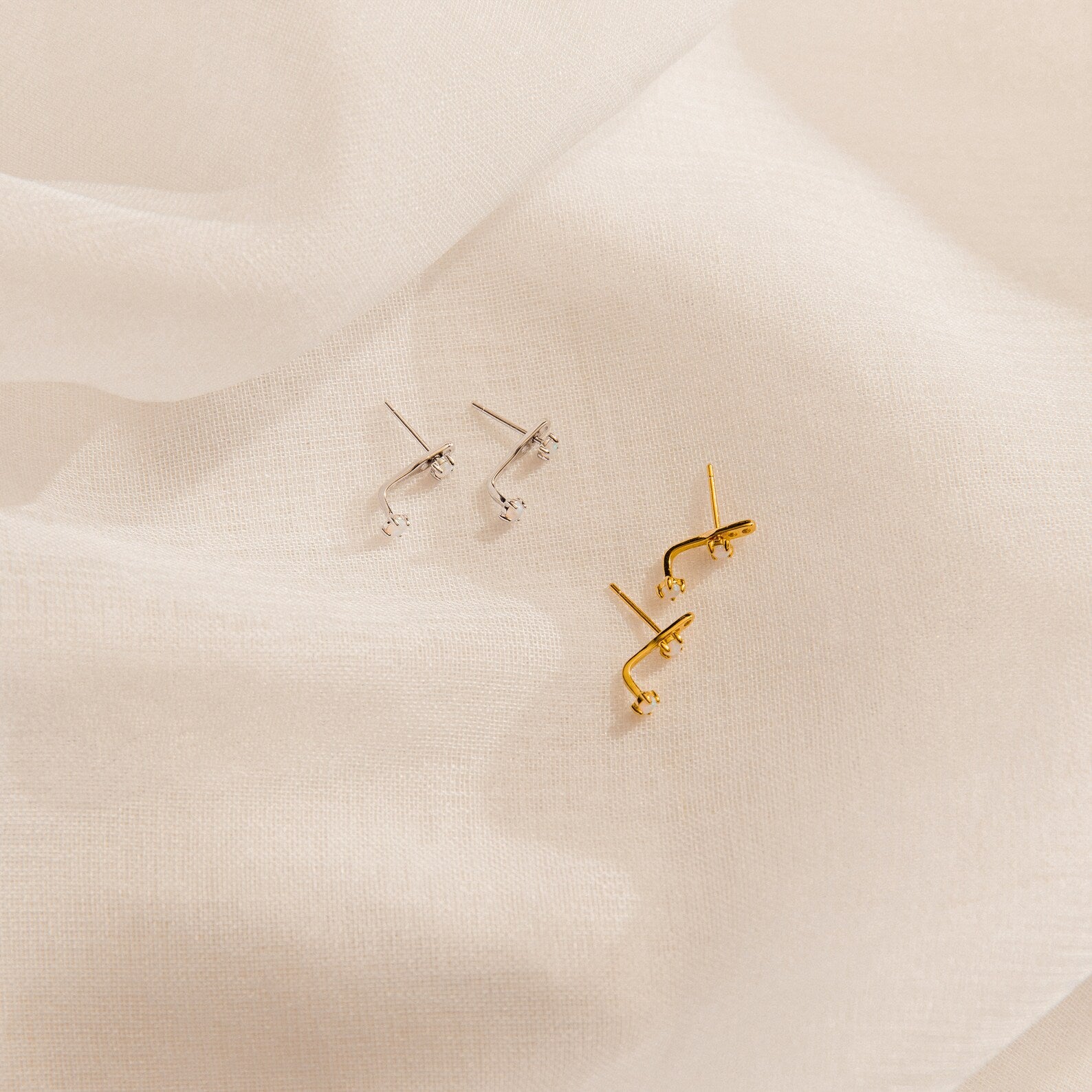 Two pairs of Opal Ear Jackets—one silver, one gold—displayed on soft white fabric. Each features removable earring posts for versatile styling.