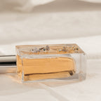 A glass perfume bottle lies on its side with four delicate Cobra Snake Huggies resting gracefully on top.