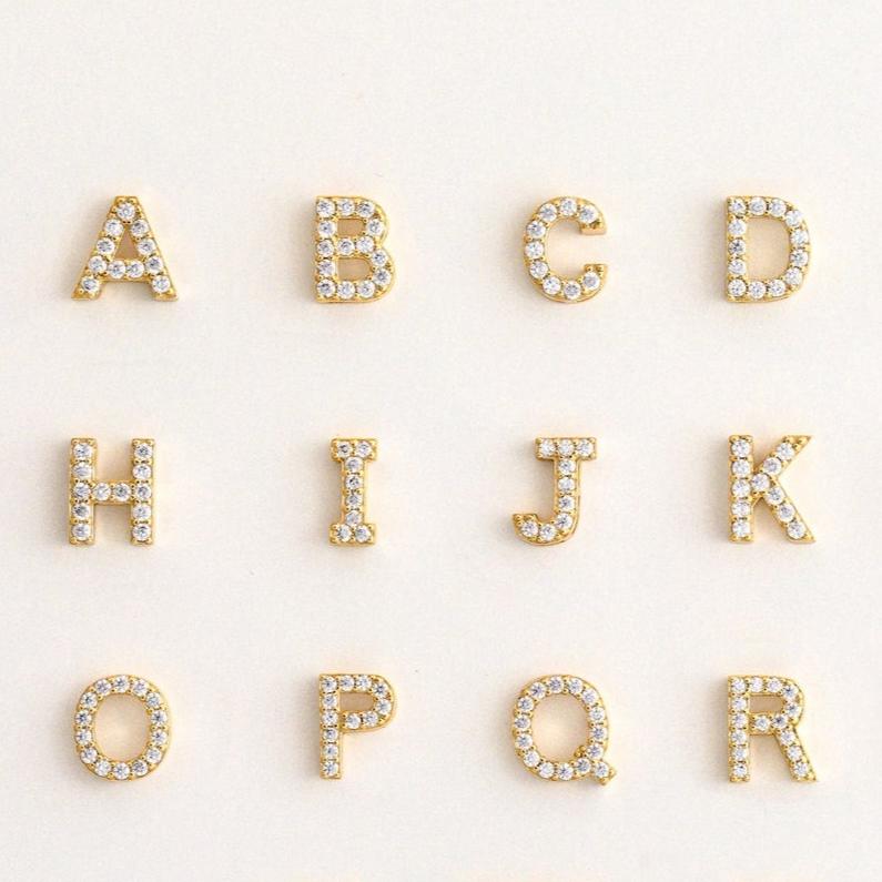 The Floating Pave Initial Necklace features gold letters A, C, H, I, J, K, O, P, Q, and R adorned with clear gemstones—adding sparkling style to any personalized jewelry collection.