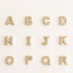 The Floating Pave Initial Necklace features gold letters A, C, H, I, J, K, O, P, Q, and R adorned with clear gemstones—adding sparkling style to any personalized jewelry collection.