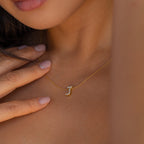 A woman wearing the Floating Pave Initial Necklace with a jeweled letter J pendant, gently touching her collarbone—a stunning personalized jewelry piece.