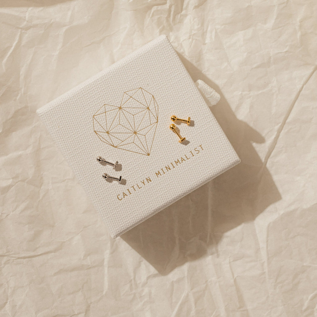 A pair of Jocelyn Diamond Studs in 18K Gold features a minimalist design and ball back, presented on a textured box embossed with GALLIV MINIMALIST.