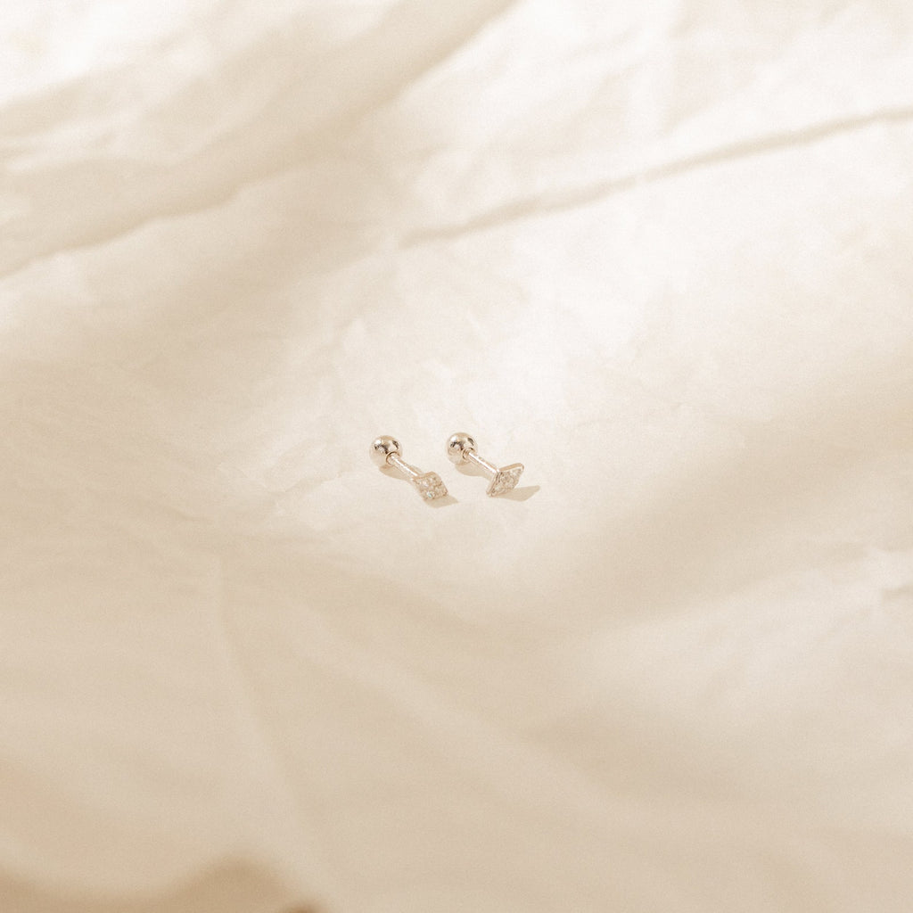 The Jocelyn Diamond Studs in Sterling Silver rest on softly lit, crumpled white fabric—perfect small silver earrings to elevate your everyday earring stack.