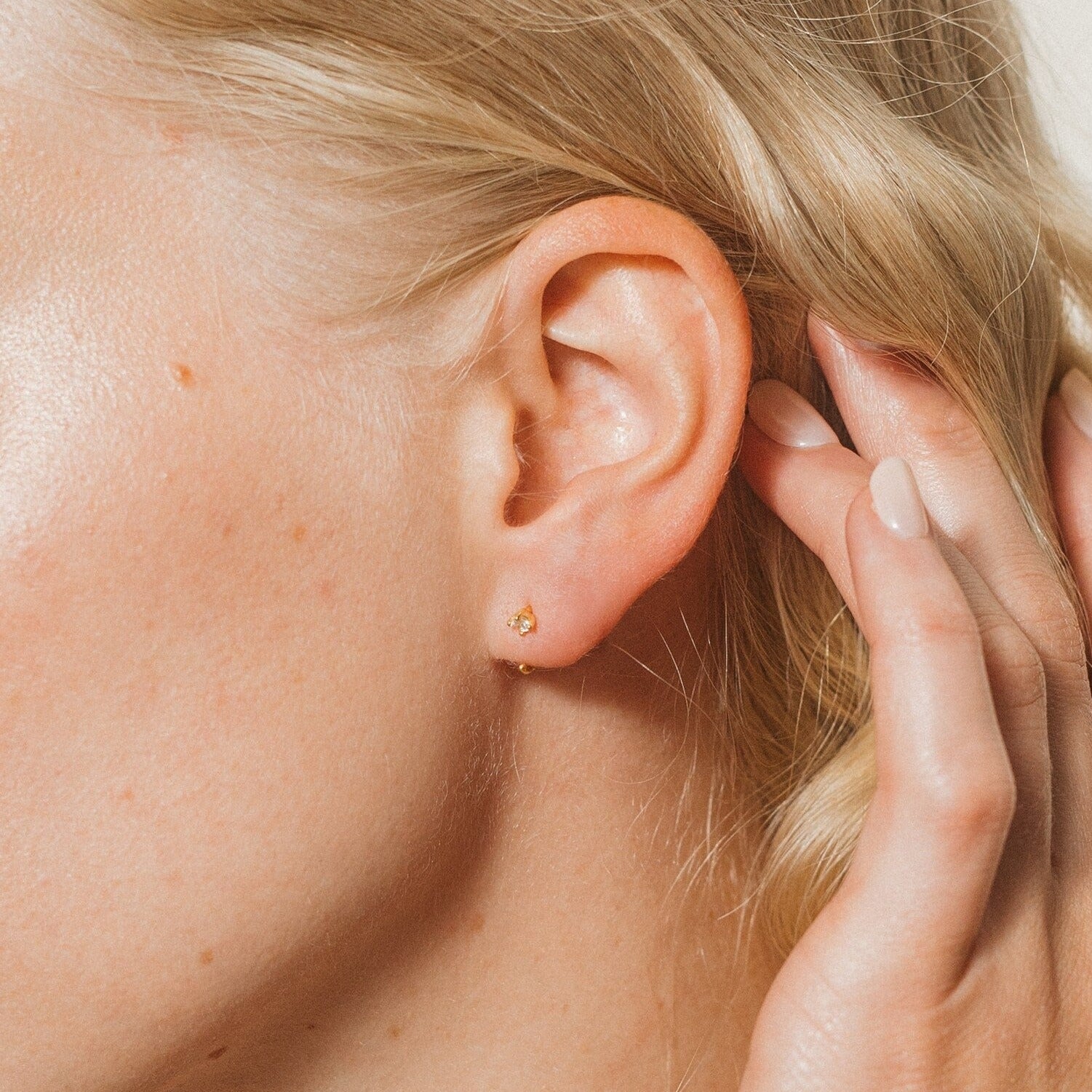Close-up of a woman's ear wearing Saylor II Huggies, with her hand touching her hair—perfect everyday earrings that add a subtle, elegant touch to any look.