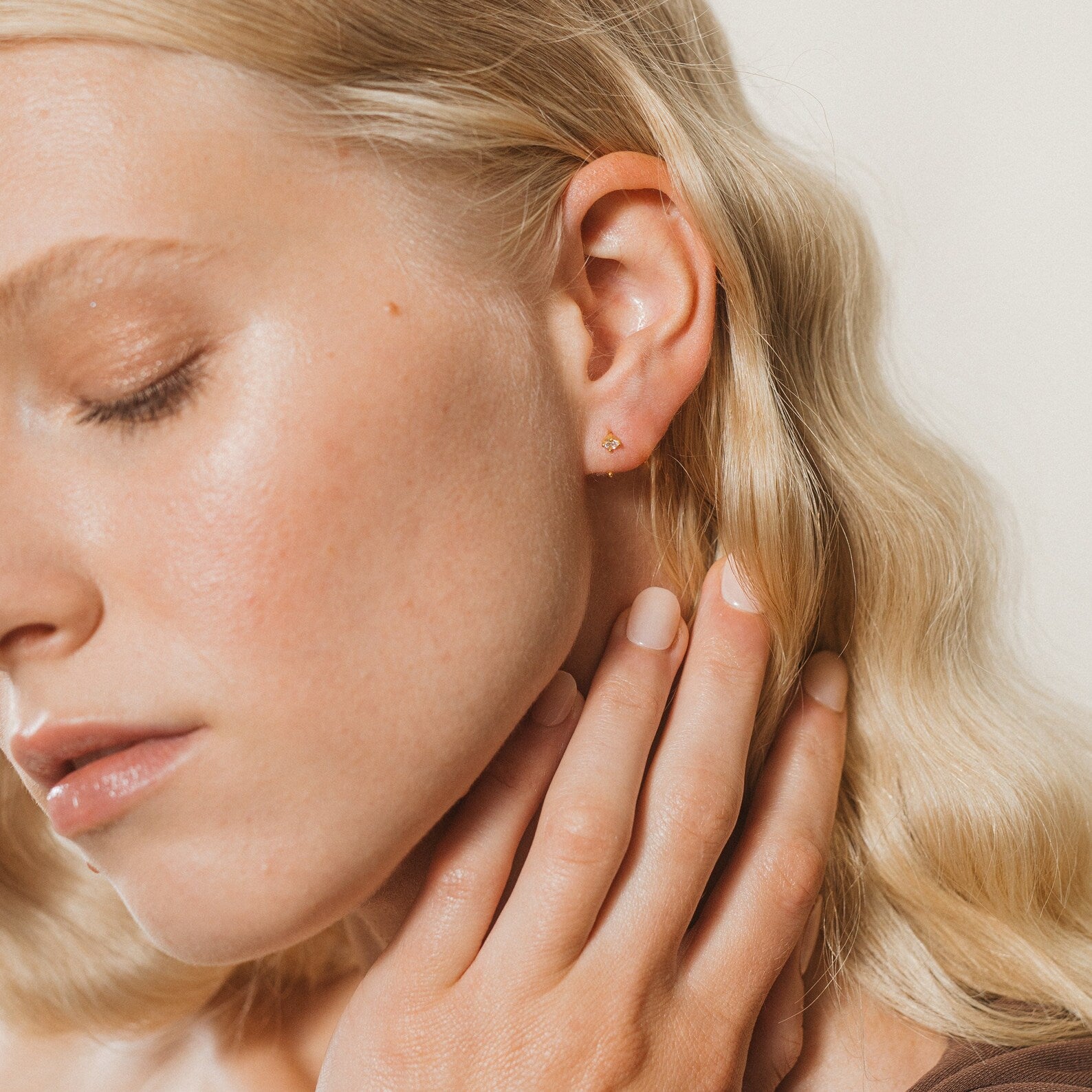 Woman with wavy blonde hair touches her neck, eyes closed, wearing Saylor II Huggies that add a subtle touch of elegance to her everyday look.