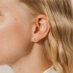 Close-up of a woman's ear wearing Saylor III Huggies, stylish small gold earrings ideal for everyday wear, with wavy blonde hair.