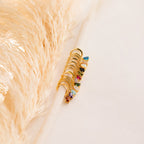 Pave Birthstone Drop Huggies with colorful gemstones hang on a white rod, pampas grass in the background, evoking elegance and the chic style of gemstone hoop earrings.