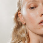 Close-up of a woman with wavy blonde hair wearing the Lucky Studs Set: a small gold hoop and a delicate wishbone earring in her left ear.