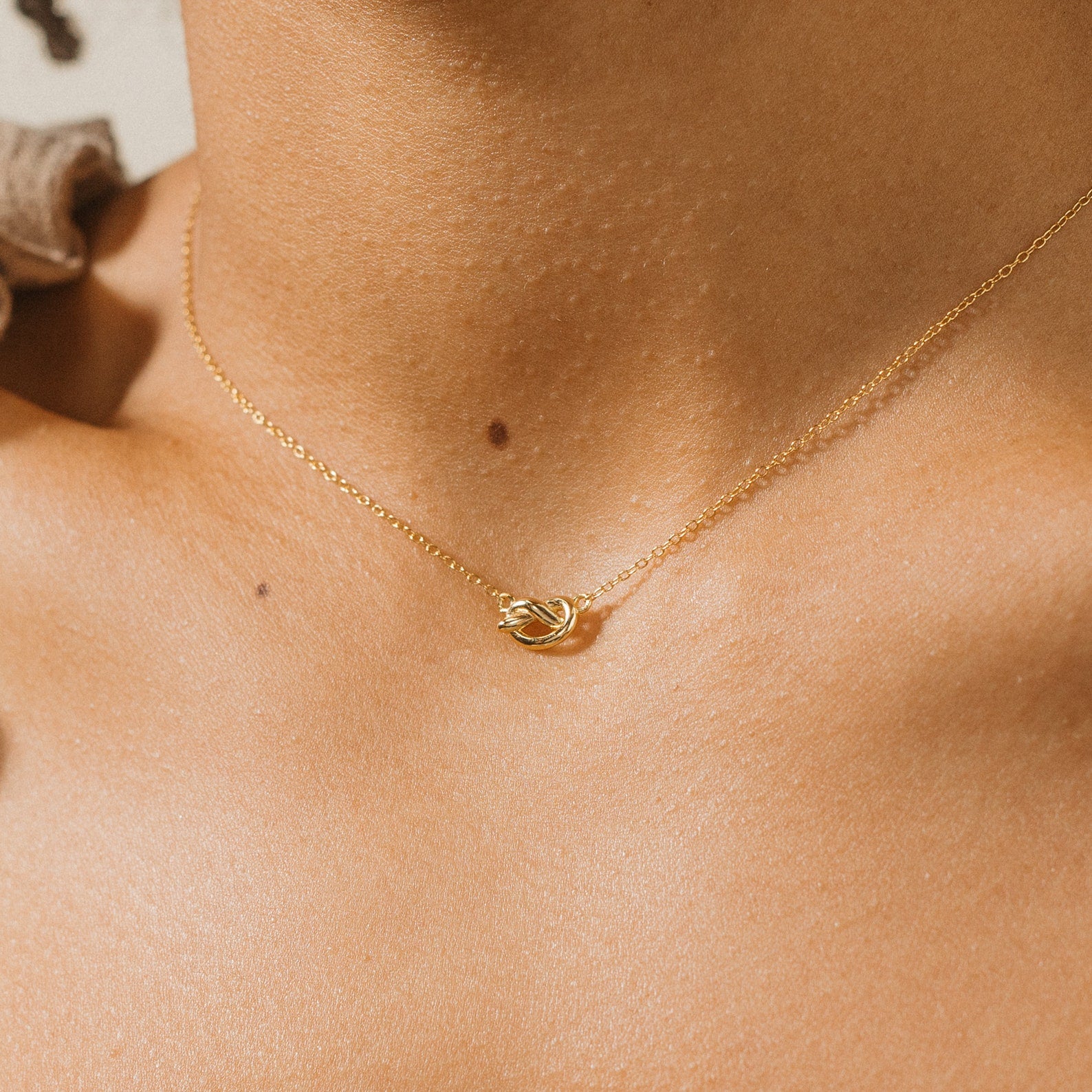 Close-up of a person wearing the Love Knot Necklace, featuring a gold chain with a small knot pendant—ideal as unity jewelry or a meaningful wedding gift.