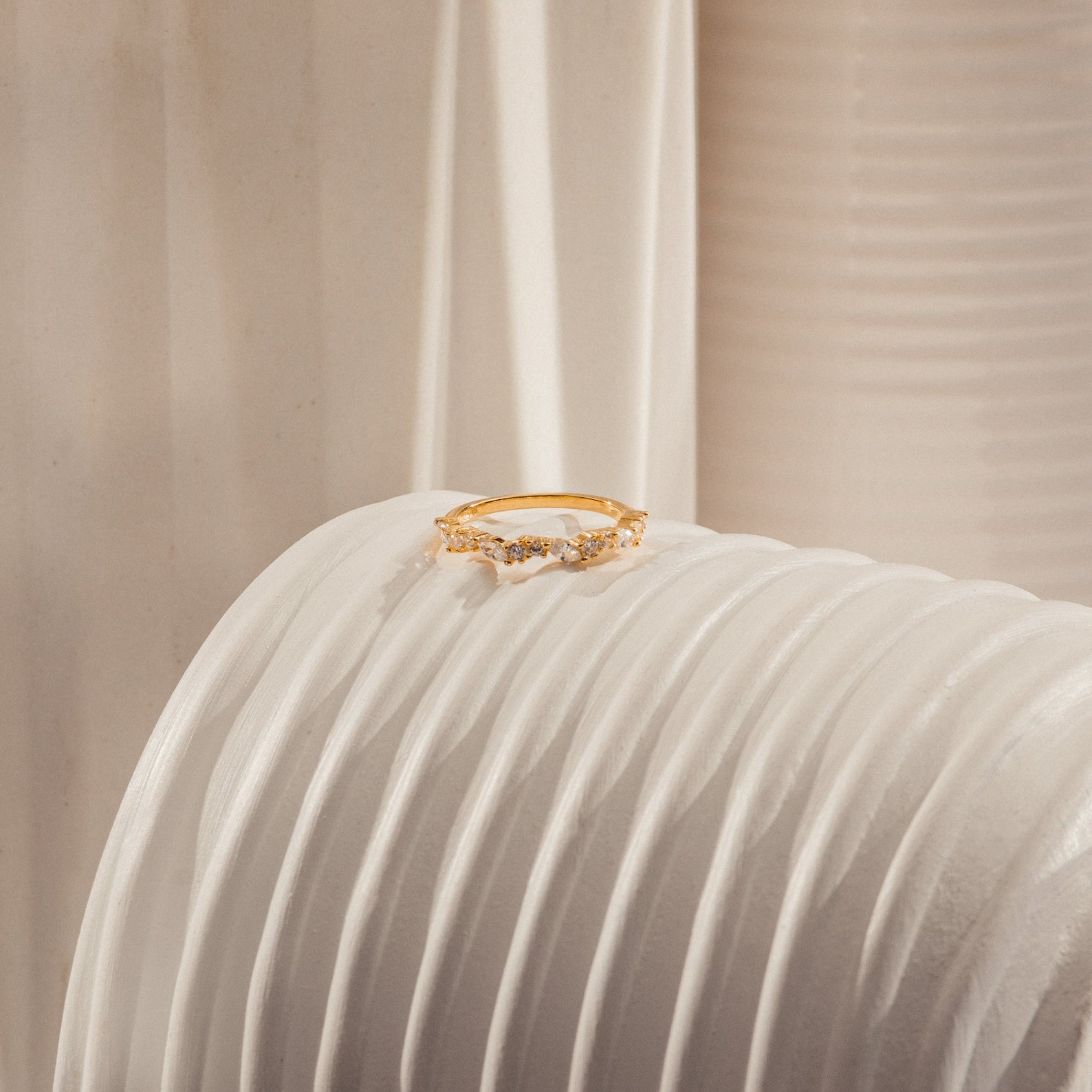 The Verity Diamond Ring, a cluster-style gold band adorned with small diamonds, is showcased on a textured white surface against a soft, neutral background.