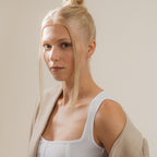 A blonde woman in a white top and beige blazer gazes at the camera against a neutral background, her minimalist glam look accented by Opal Heart Studs.
