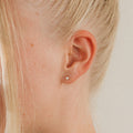 Close-up of a woman's ear with blonde hair wearing Opal Heart Studs—dainty, minimalistic earrings that add a subtle touch of elegance.