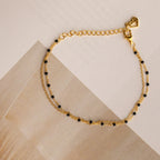 The Calypso Station Bracelet is a delicate gold bracelet with small black beads and a heart-shaped charm, ideal for stacking or pairing with your favorite boho accessories, shown on a neutral background.