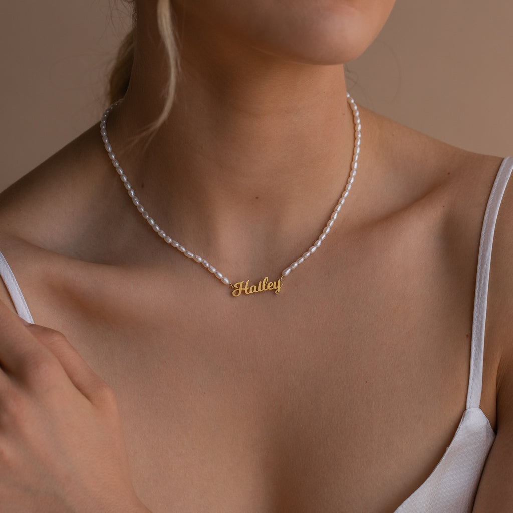 Woman wearing the Mellow Pearl Name Necklace, featuring a gold Hailey name pendant and pearls, styled with a white spaghetti strap top.