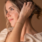 A woman with light hair wears the Calypso Station Bracelet, her hand near her head in soft lighting—an ideal choice for stacking boho accessories.