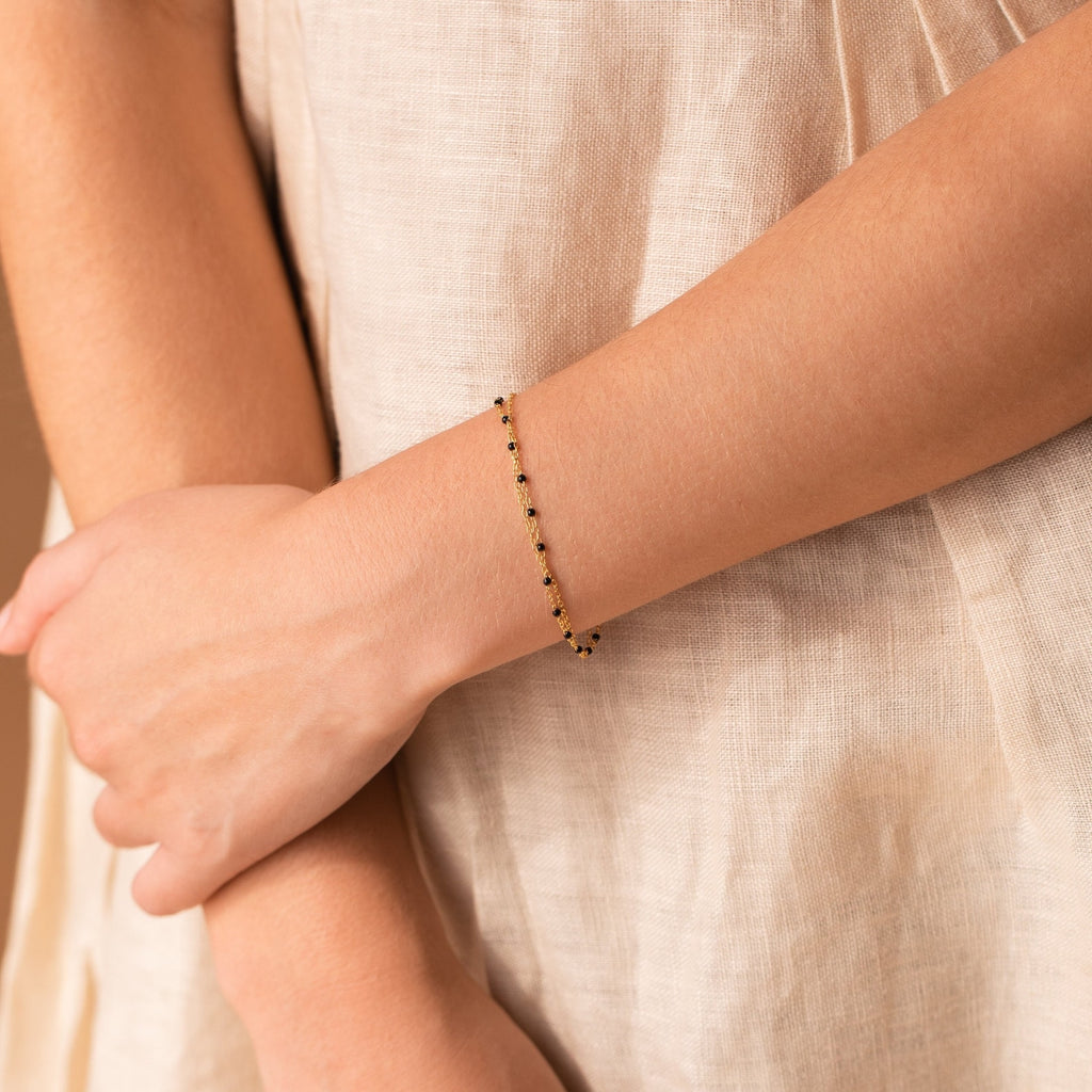 Close-up of a person wearing the Calypso Station Bracelet on their wrist with a light beige outfit—ideal for stacking this delicate boho accessory with your favorite styles.