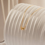 Gold chain necklace with a small knotted pendant, draped over a textured white ceramic surface in soft natural lighting.