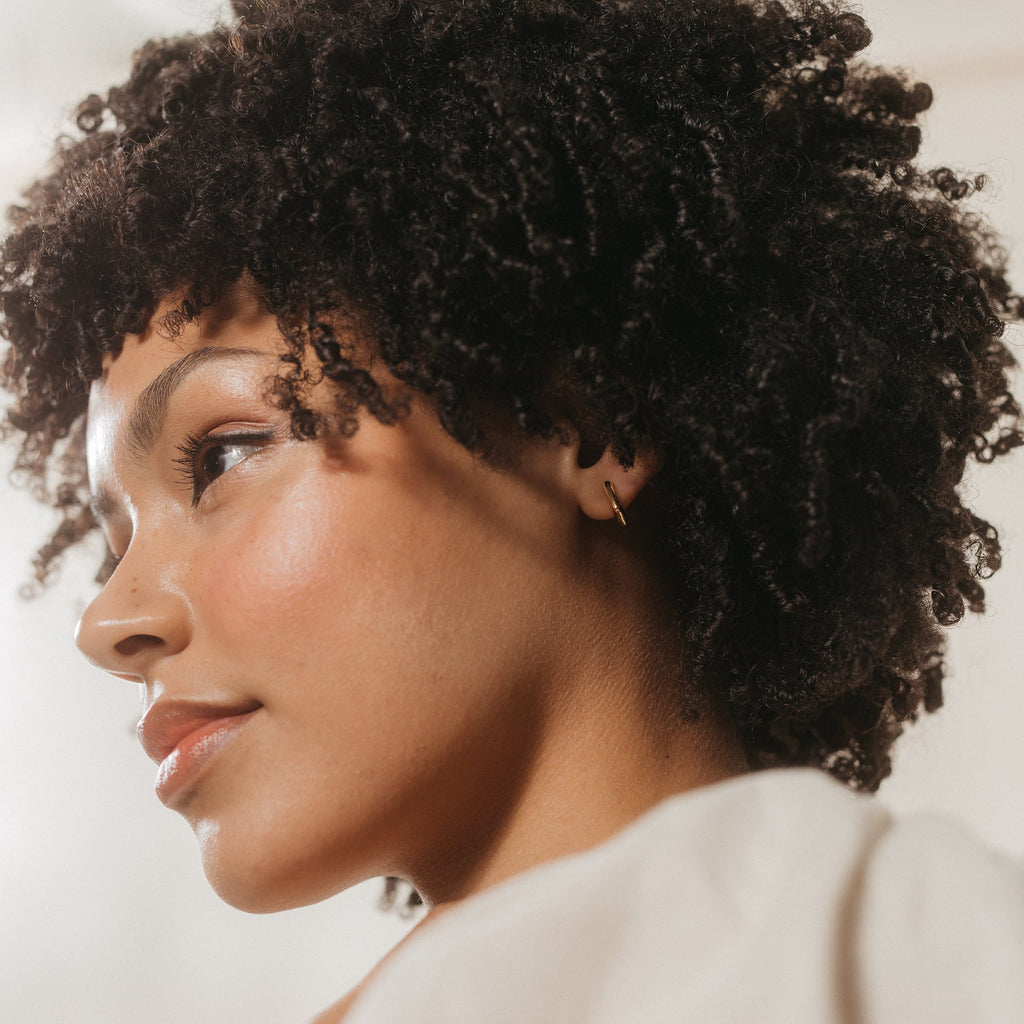 Woman with curly hair wearing Kelsey Link Earrings looks to the side, her face softly highlighted by natural light.