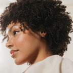 Woman with curly hair wearing Kelsey Link Earrings looks to the side, her face softly highlighted by natural light.
