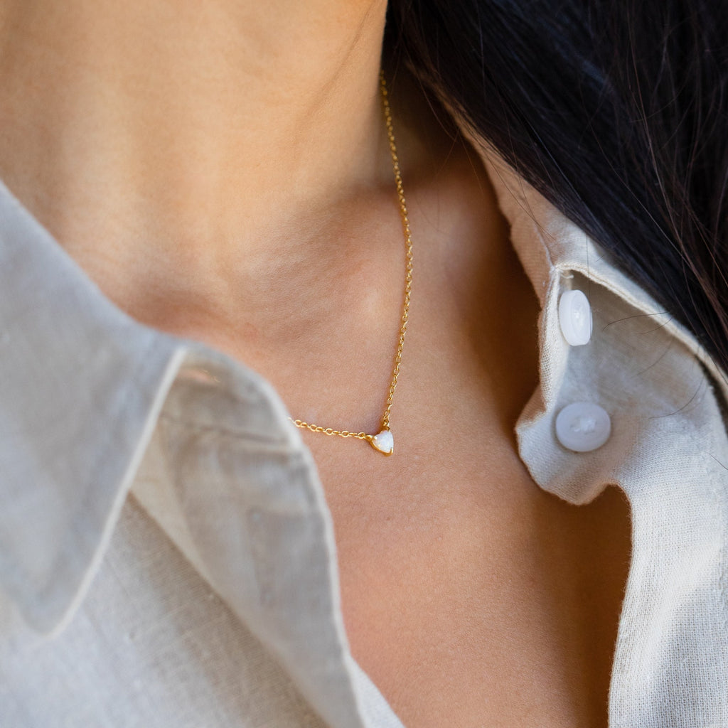 Close-up of a woman wearing the Madeline Opal Heart Necklace, a delicate gold chain with a small opal heart pendant, paired with an off-white collared shirt.