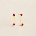 Straight‑on shot of a garnet pair gold birthstone ear jacket set—two small round CZ stones linked by a delicate bar—laid flat on a neutral background.