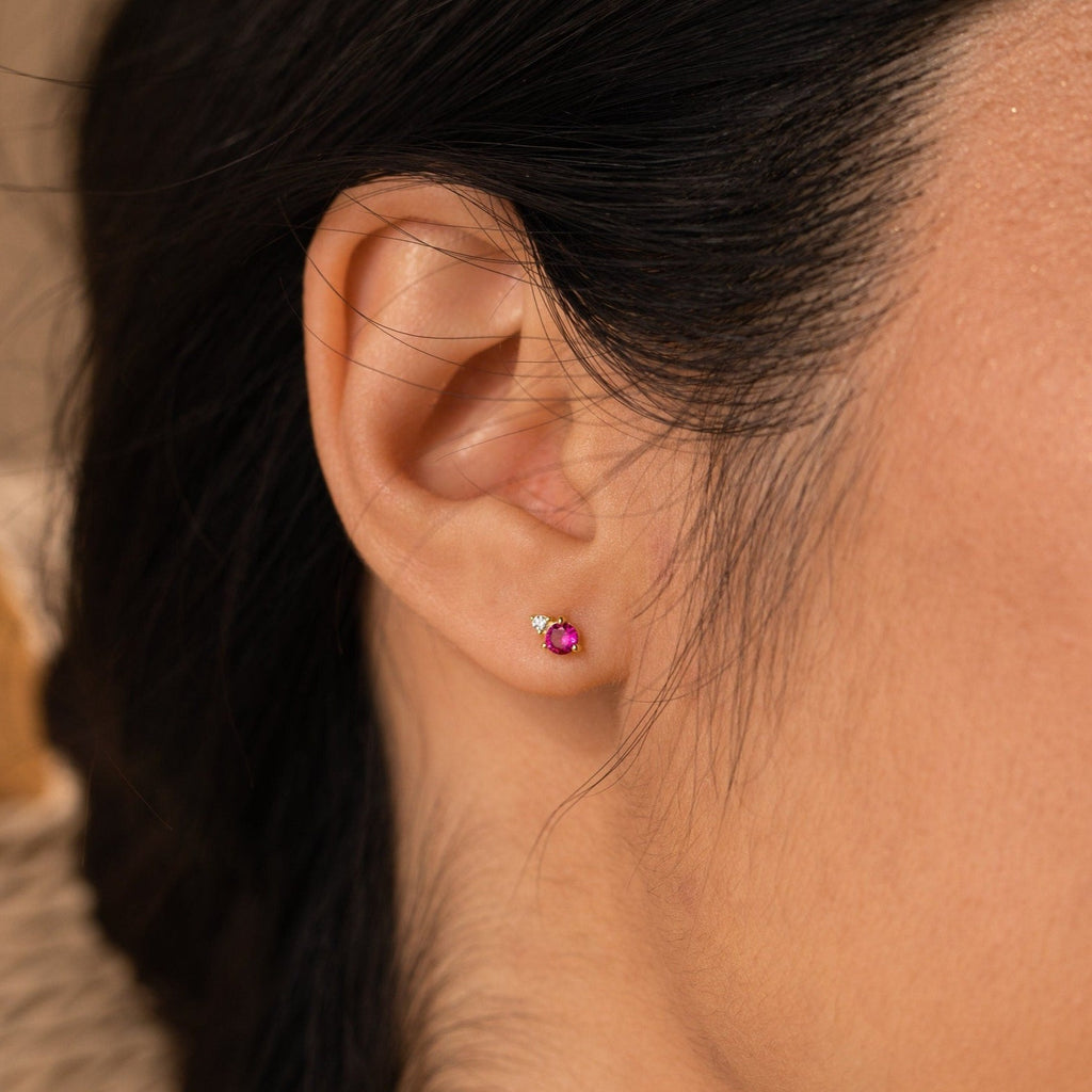 Close-up of a person’s ear wearing Raindrop Birthstone Studs: each features a small red stone accented by a tiny clear gem.