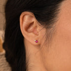 Close-up of a person’s ear wearing Raindrop Birthstone Studs: each features a small red stone accented by a tiny clear gem.