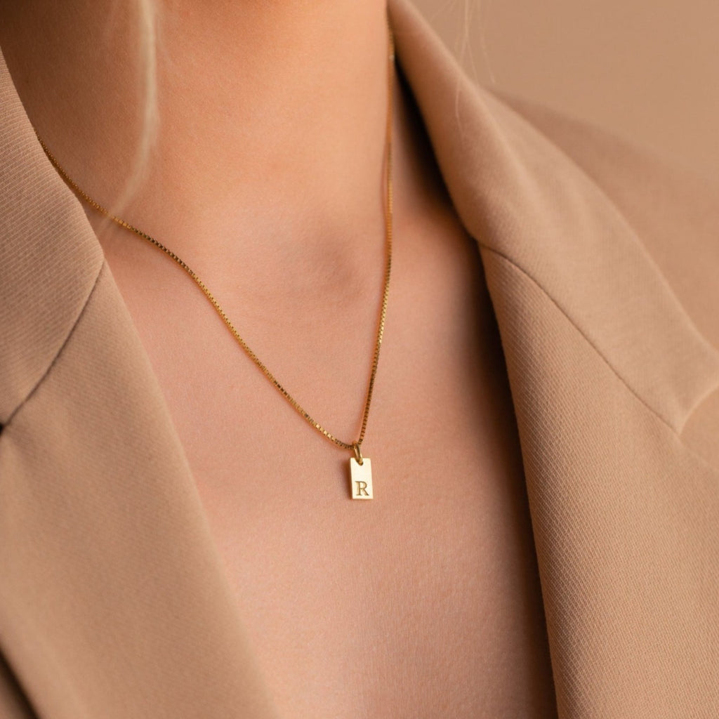 The Mini Initial Tag Necklace, featuring your chosen letter pendant and shown styled over a beige blazer, makes a thoughtful personalized Christmas gift.