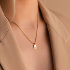 The Mini Initial Tag Necklace, featuring your chosen letter pendant and shown styled over a beige blazer, makes a thoughtful personalized Christmas gift.