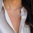 A woman wears the Madeline Opal Heart Necklace, featuring a dainty gold chain and small heart pendant, paired perfectly with a beige button-up shirt.