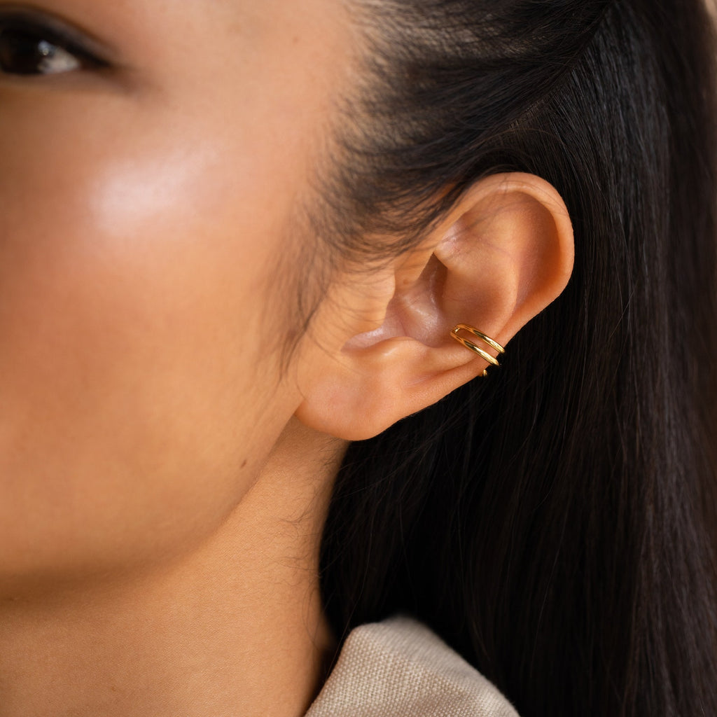 Close-up of a woman's ear adorned with a small gold Claw Ear Cuff, highlighting her smooth skin and straight dark hair.