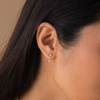Close-up of a woman’s ear wearing a opal gold birthstone ear jacket. The main stud sits on the lobe while the matching gemstone peeks just below the ear, creating a subtle layered effect.