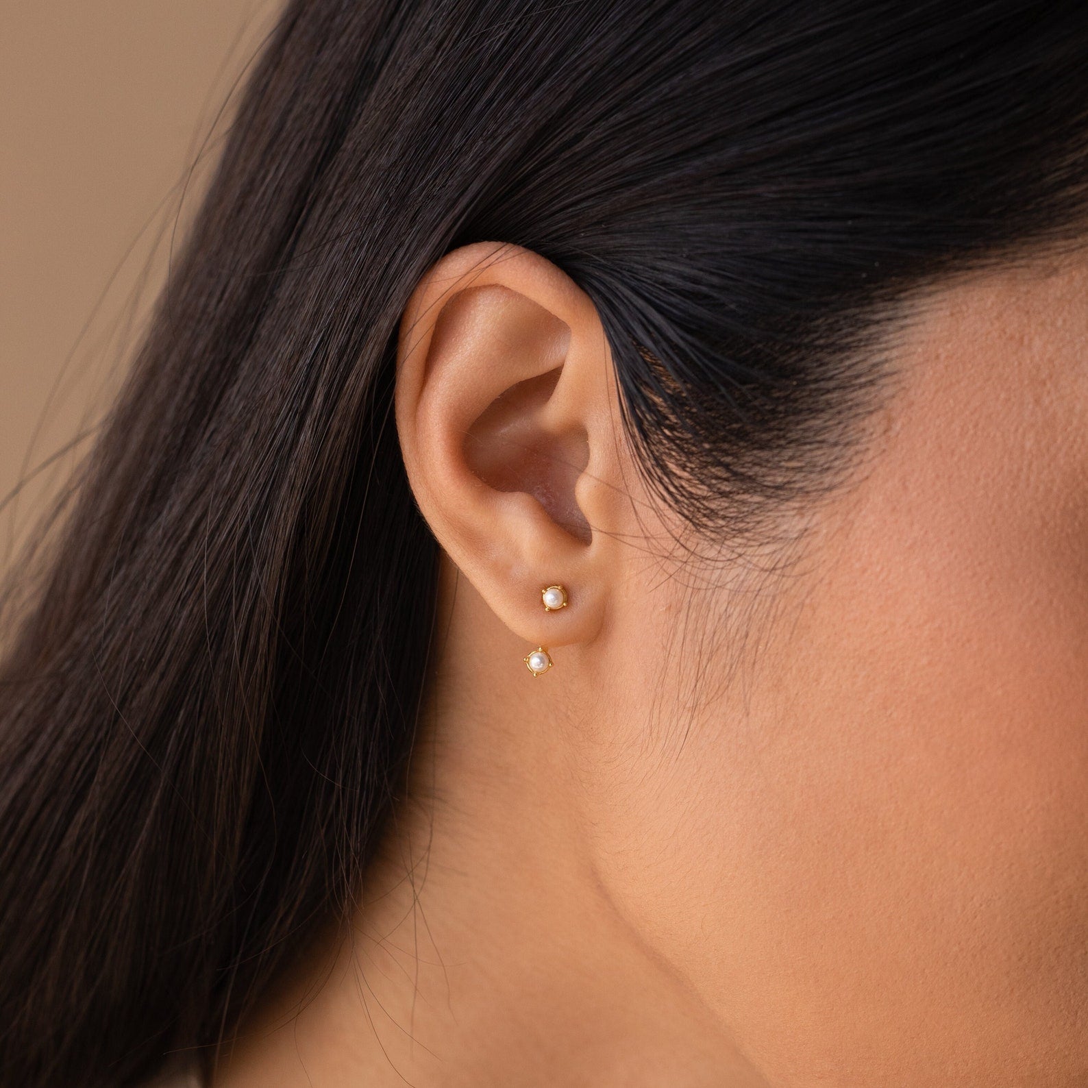 Close-up of a woman’s ear wearing a opal gold birthstone ear jacket. The main stud sits on the lobe while the matching gemstone peeks just below the ear, creating a subtle layered effect.