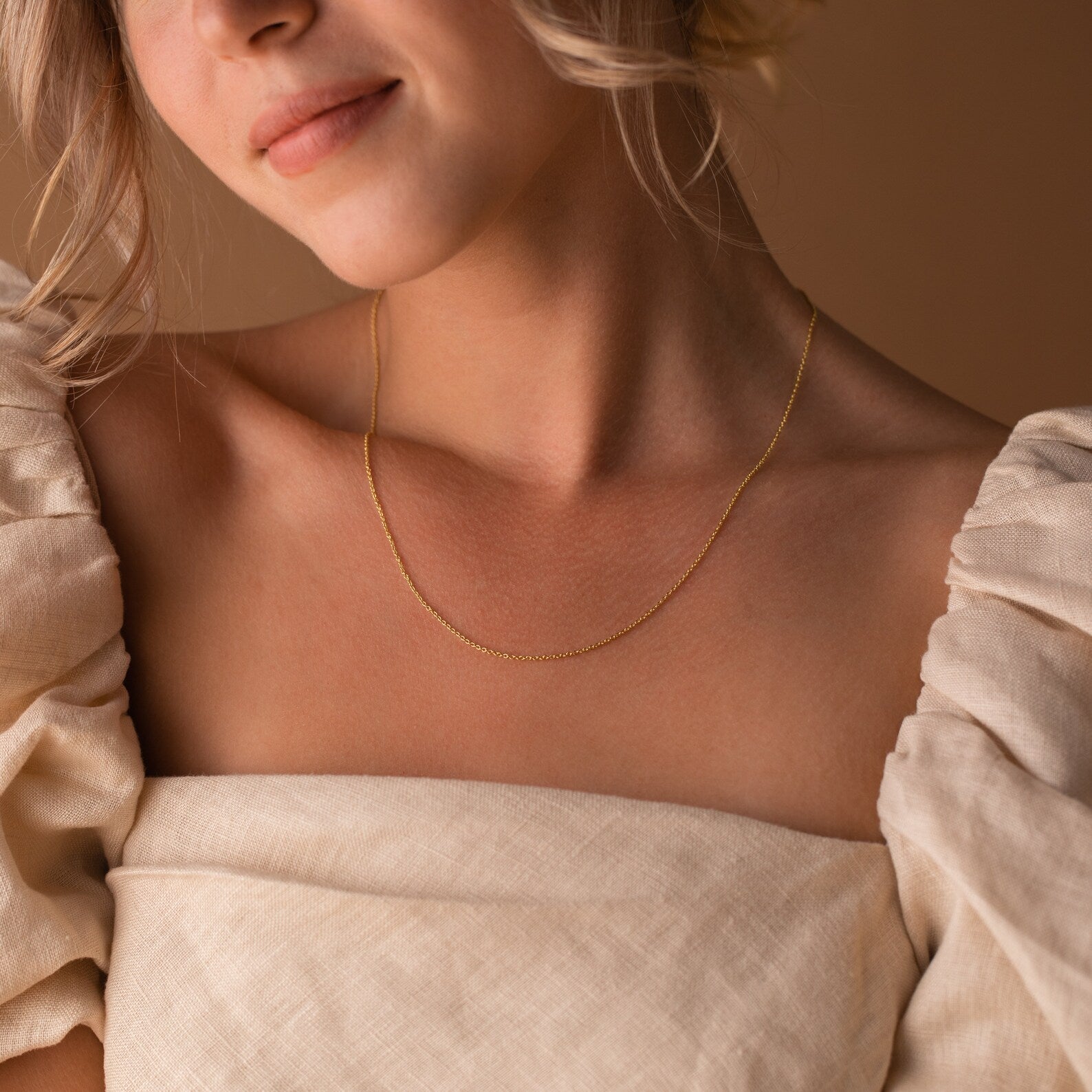 A woman in an off-shoulder beige top wears the Dainty Chain Necklace, with soft lighting highlighting her minimal style.