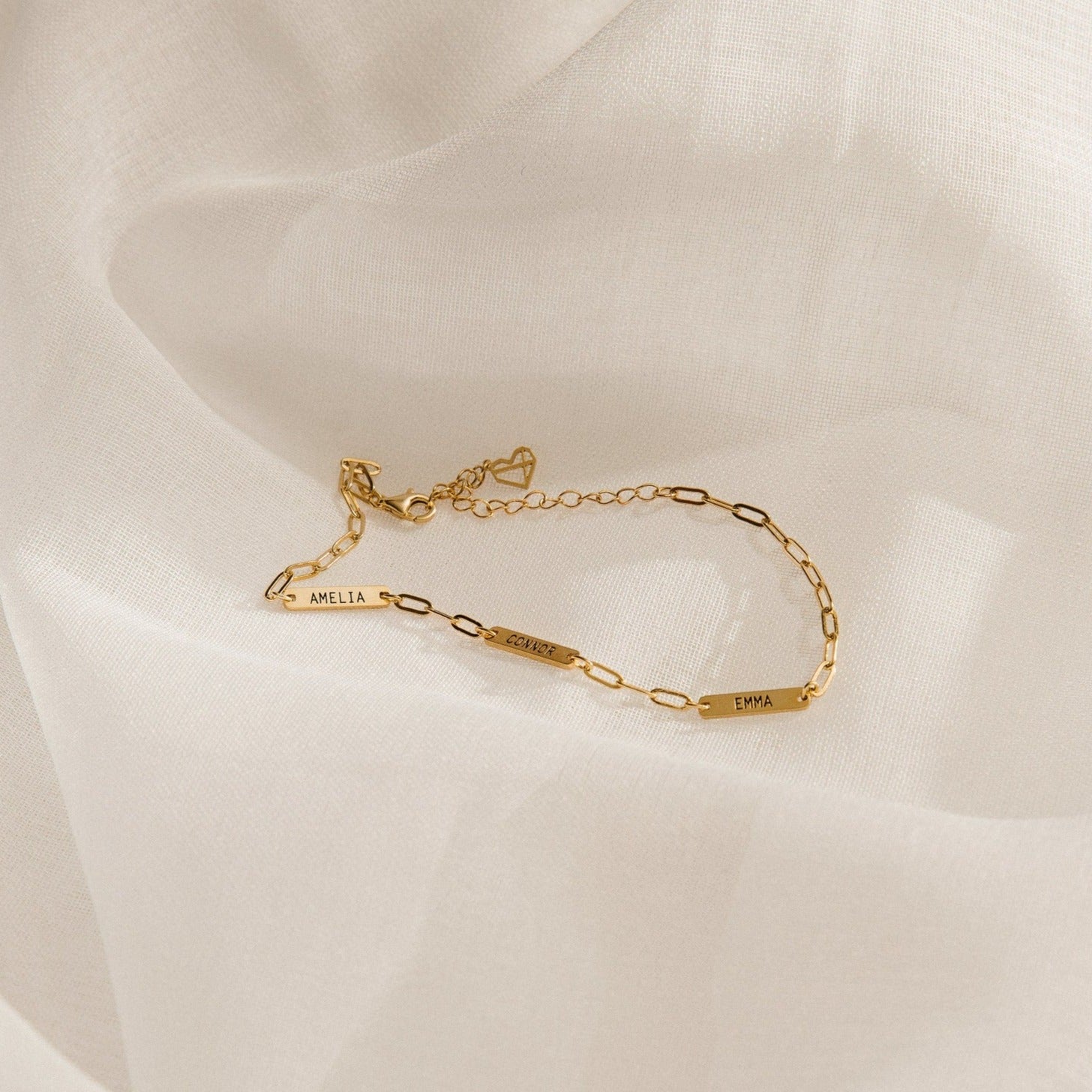 Mini Name Bar Bracelet featuring three personalized bar nameplates—AMELIA, SOPHIE, and EMMA—on a gold paperclip chain, displayed on a white fabric background; a perfect custom gift for someone special.
