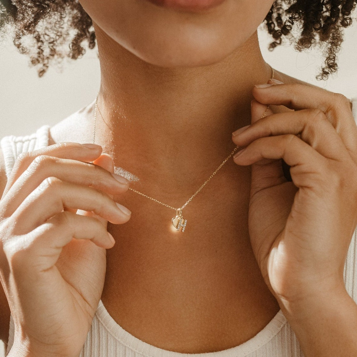 A woman wearing a white ribbed top showcases the Pave Initial Heart Necklace.