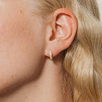 A close-up of a woman's ear shows the Clarissa Pave Huggies—small gold hoops that sparkle against her wavy blonde hair, making them perfect for date night jewelry.