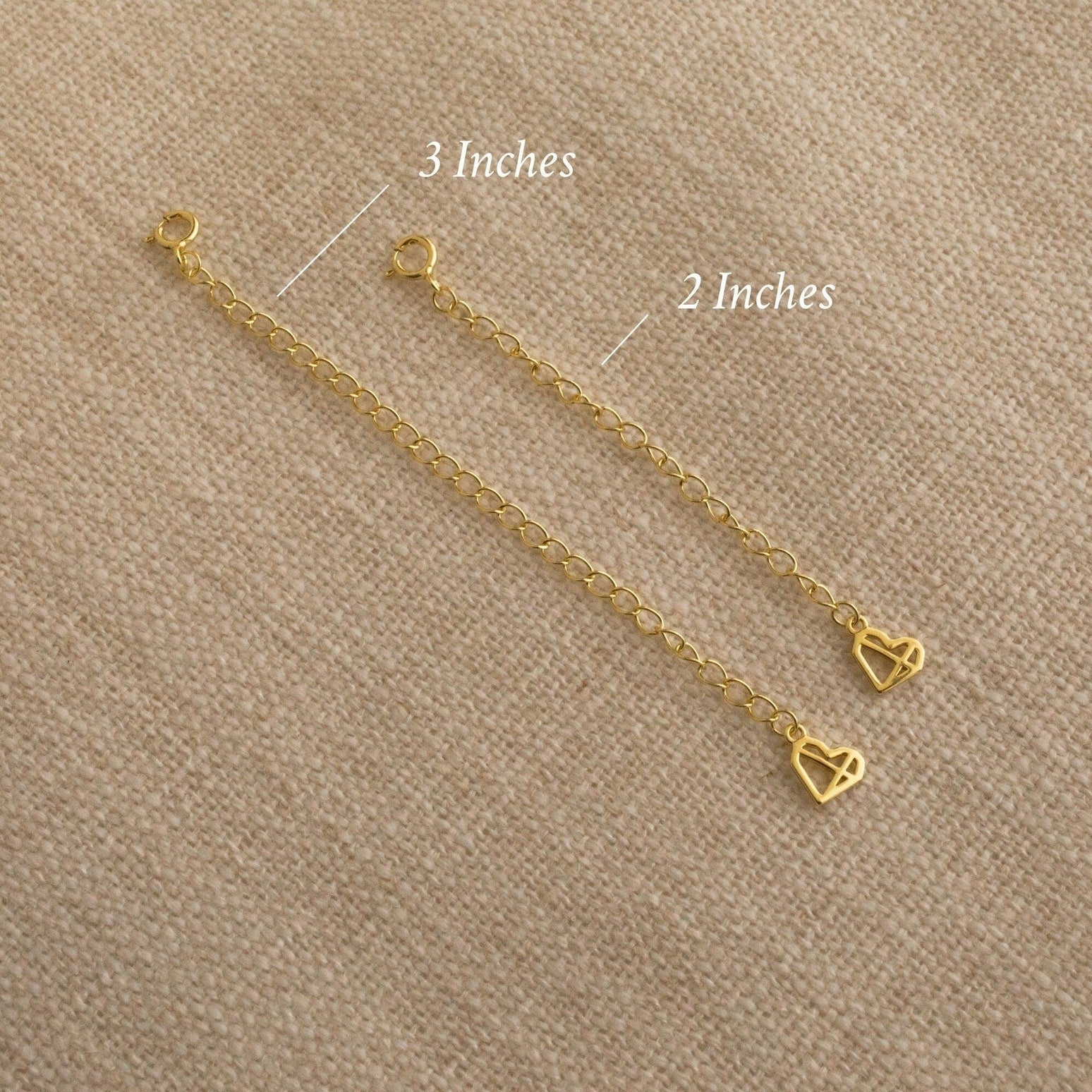 Two Chain Extender gold adjustable chains with heart charms, sized 3" and 2", are displayed on beige fabric—ideal for lengthening your favorite necklaces or bracelets.