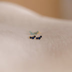 Bella Birthstone Studs, featuring small gold settings with blue gemstones, rest on a soft, light-colored fabric—an elegant gift for mothers and daughters.