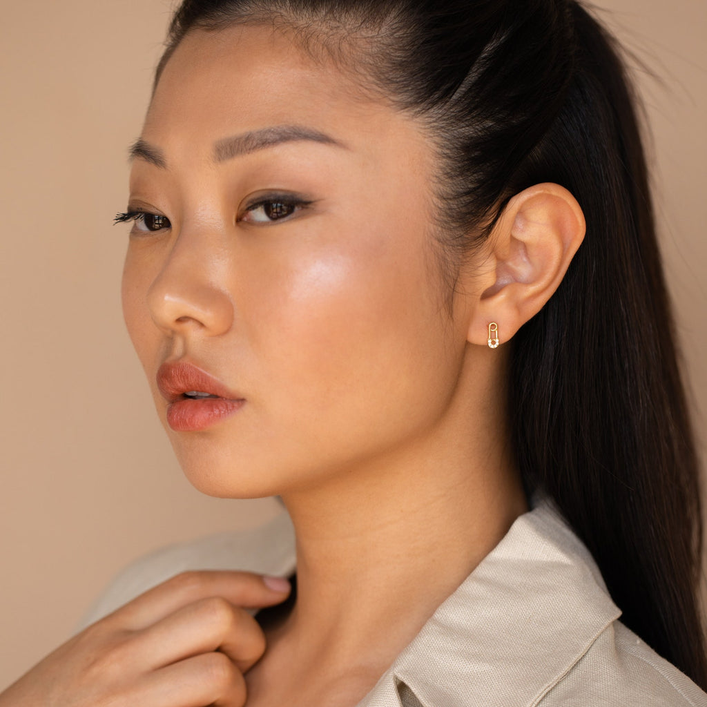 A woman with long hair in a ponytail, wearing Tiny Pave Safety Pin Studs.