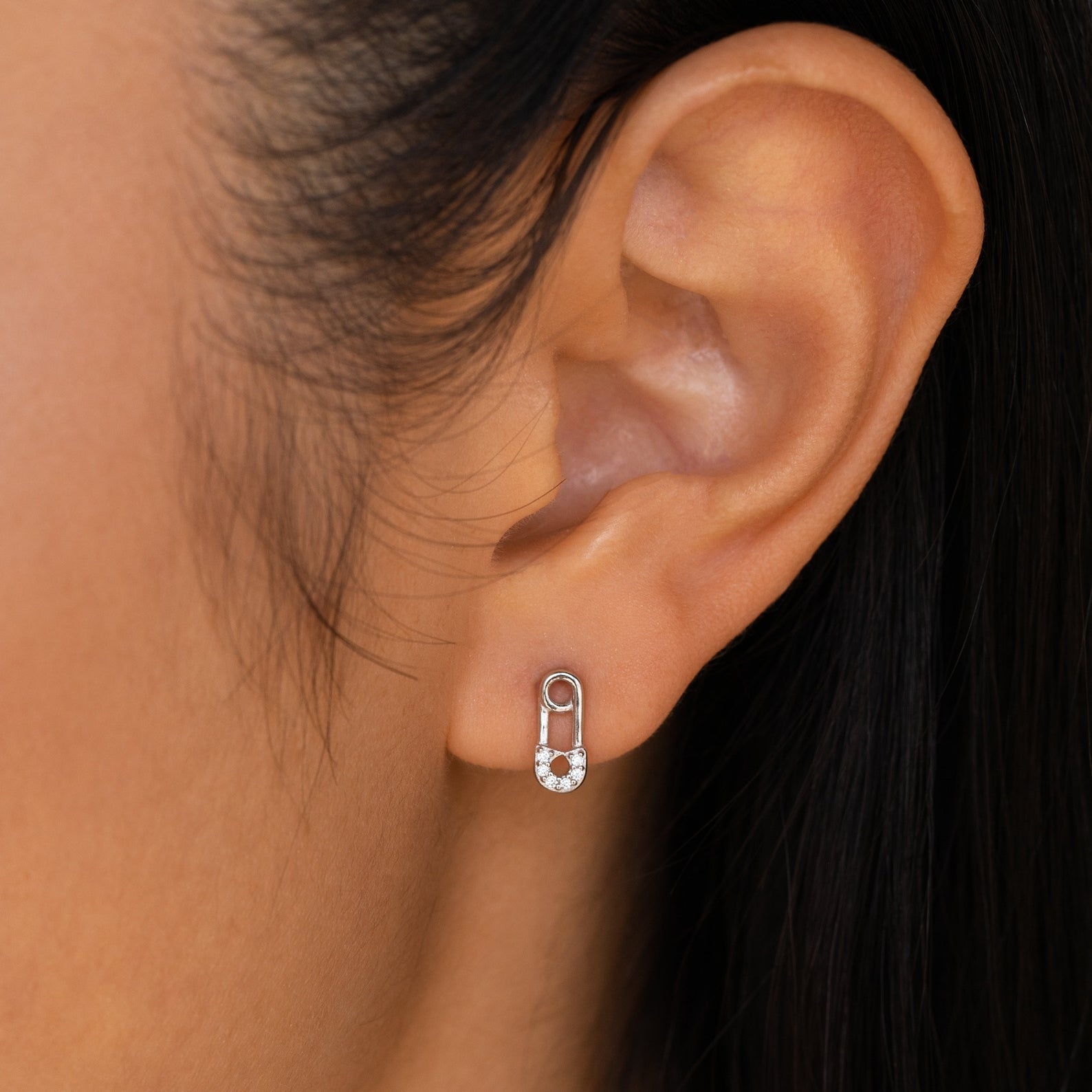 Close-up of an ear wearing Tiny Pave Safety Pin Studs, featuring silver safety pin design with small CZ diamond gemstones adorning the lower half.