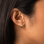 Close-up of a woman's ear wearing Athena Blue Zircon Huggies, gold hoop earrings with a striking blue gem—an ideal choice for fans of personalized jewelry.